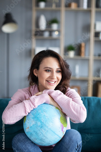 Beautiful attractive woman on couch holding globe and dreaming vacation.