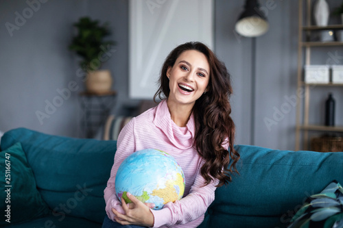Smiling woman with model of the globe at home.