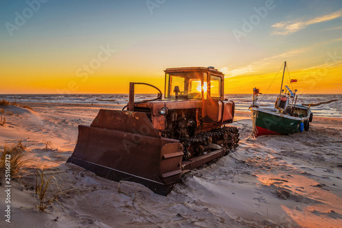 a boat stands by the sea, a tractor as the sun barks