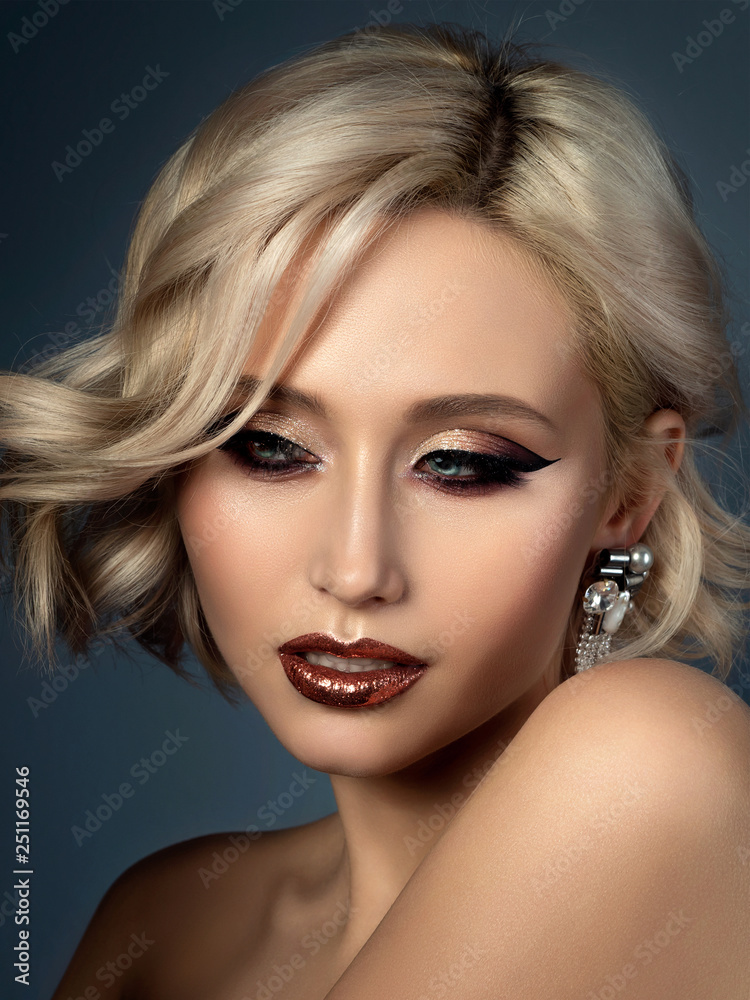 Fototapeta premium Portrait of young beautiful woman with evening make up. Modern fashion eyeliner wing and glitter on her lips. Studio shot.