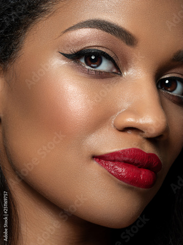 Portrait of young beautiful african woman with evening make up. Red lips, golden eyeshades and black eyeliner. Classic makeup concept. Studio shot. Extreme closeup, partial face view photo