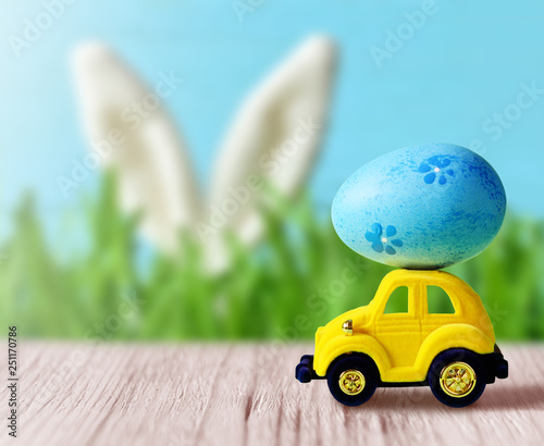 Retro toy car with Easter egg on the roof on spring background. Easter concept.