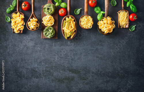 Various pasta on wooden spoons over stone background