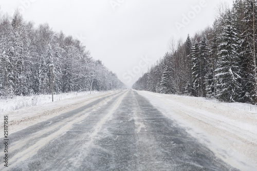 winter road with ice on the asphalt, trees under snow during the winter frost in Russia © miklyxa