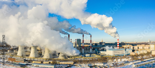 power plant pipes and cooling towers on the background of the panorama of the winter city against blue sky.