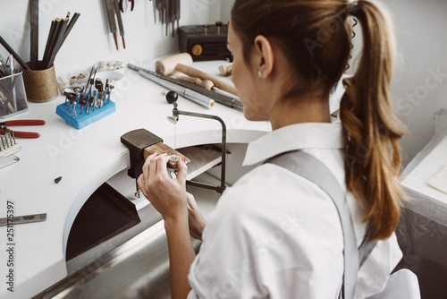 Focused on work. Side view of young female jeweler making a ring at her workbench. photo