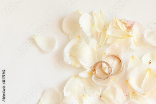 Beautiful toned picture with wedding rings lie on white against the background of flowers