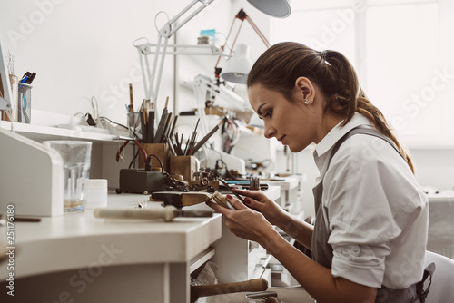 Focused on a process. Portrait of young female jeweler focused on creating a silver ring at her modern workbench. photo