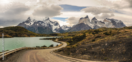 Dirt road leading around the lake to stunning Cuernos del Paine in Patagonia. Torres del Paine National Park, Patagonia, Chile the mountain scenery under the cloudy rainy and blue sky. Travelling.