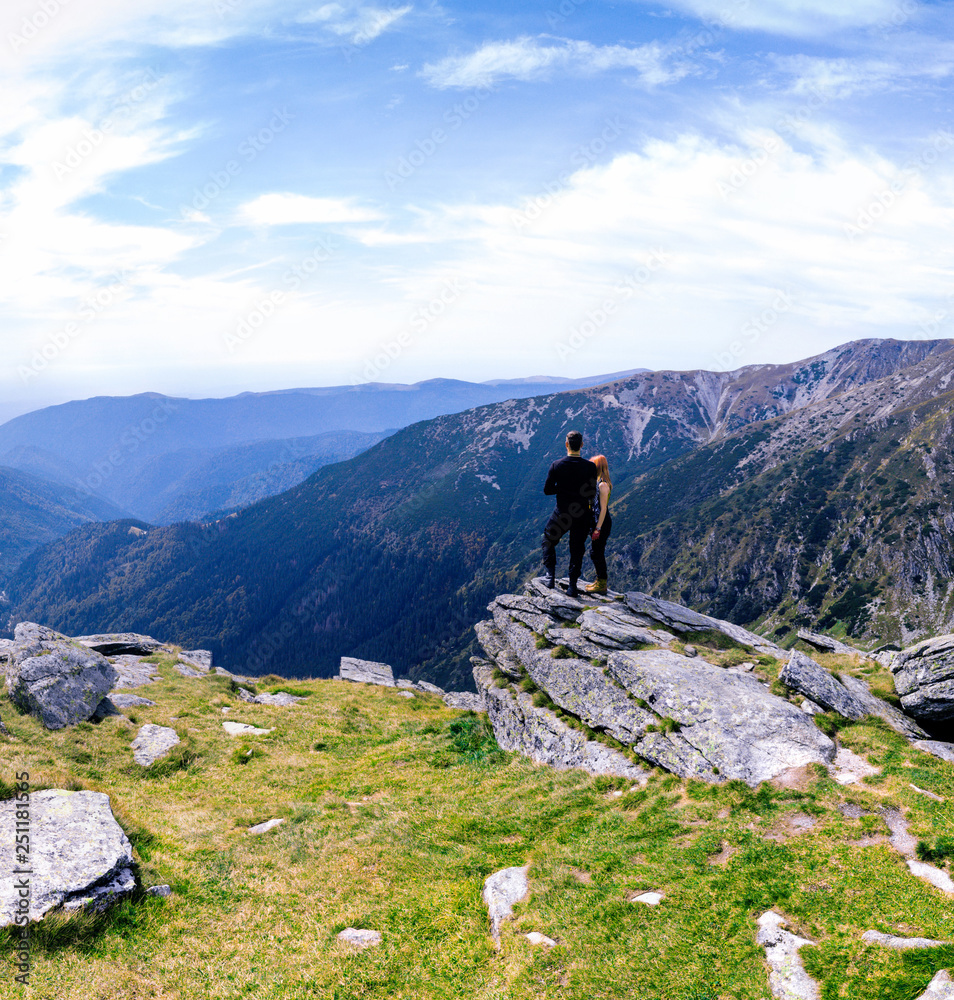 Back view of tourist couple, man and girl stand on rocky mountain top enjoying breathtaking summer mountain panorama. Tourism, traveling and healthy lifestyle concept. motorcyclists, square photo Back view of tourist couple, man and girl stand on rocky mountain top enjoying breathtaking summer mountain panorama. Tourism, traveling and healthy lifestyle concept. motorcyclists, square photo
