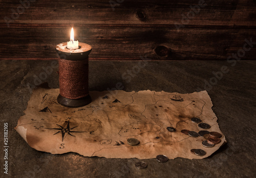 Фотография old pirate map on stone table, ancient candle, many different coins, map of trea