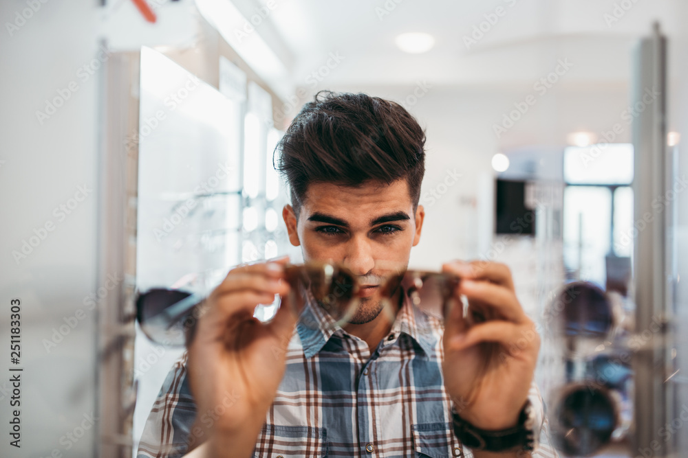 Handsome young man choosing eyeglasses frame in optical store. Handsome young man choosing eyeglasses frame in optical store.