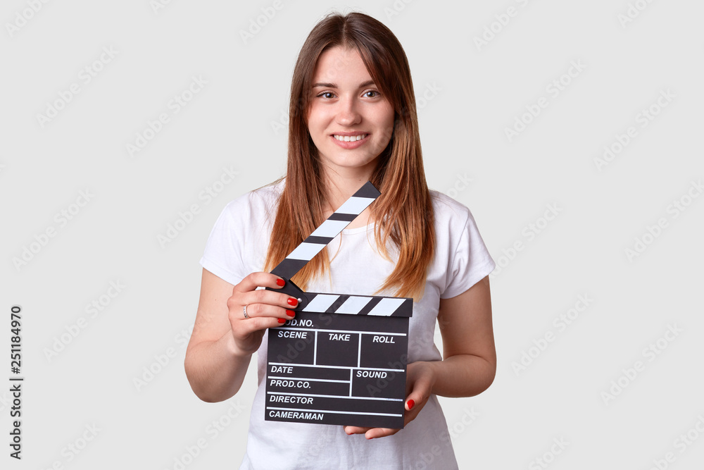 Smiling woman with gentle smile, holds movie clapper board, wears t shirt and red manicure, works on production new film, isolated over white background. Film industry concept. Actress indoor Smiling woman with gentle smile, holds movie clapper board, wears t shirt and red manicure, works on production new film, isolated over white background. Film industry concept. Actress indoor