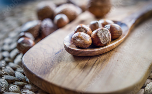 Shelled whole hazelnuts on a wooden spoon over a cheese board with mixed nuts in background