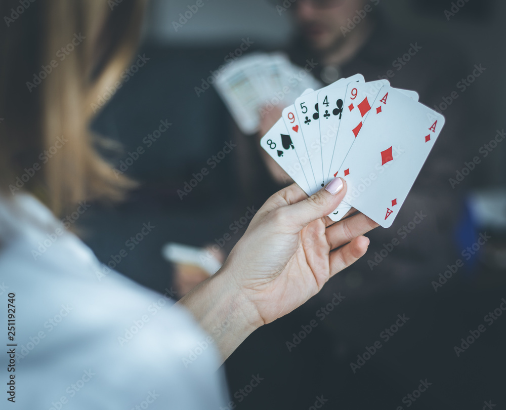 Friends are playing cards together at home. Woman is holding cards in her hands, man in the blurry background. Friends are playing cards together at home. Woman is holding cards in her hands, man in the blurry background.