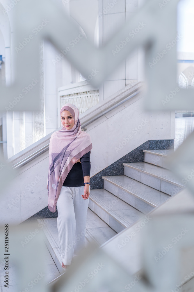 Close up portrait of happy young Asian woman wearing hijab, Islamic stylish modern fashion, smiling and posing on stairs with pattern frame at Shah Alam Mosque. Close up portrait of happy young Asian woman wearing hijab, Islamic stylish modern fashion, smiling and posing on stairs with pattern frame at Shah Alam Mosque.