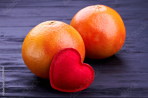 Two whole grapefruits on black backgeround. Fresh tropical fruits and red heart on dark wooden background close up. photo