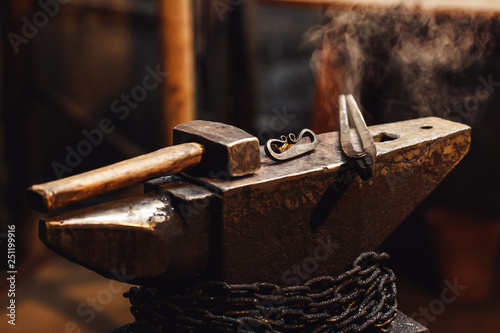 closeup of a blacksmith anvil with a hammer, tongs and firesteel. photo