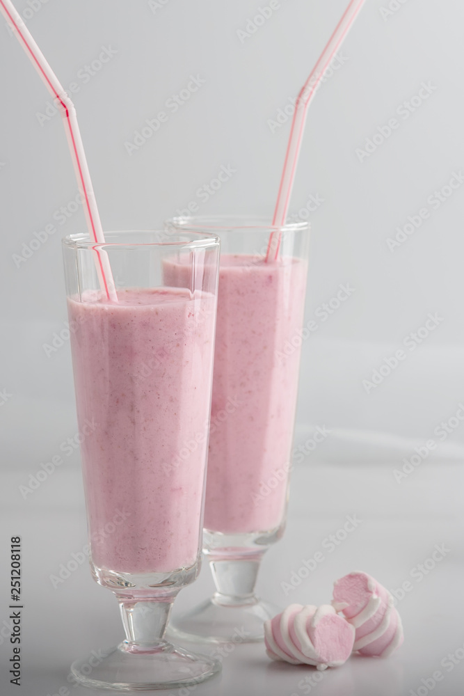Cocktail fruit and berry delicate pink is in glasses with straws and marshmallows. Strawberry smoothie poured in two glasses, standing on the table. Light key, white and pink colors. Cocktail fruit and berry delicate pink is in glasses with straws and marshmallows. Strawberry smoothie poured in two glasses, standing on the table. Light key, white and pink colors.