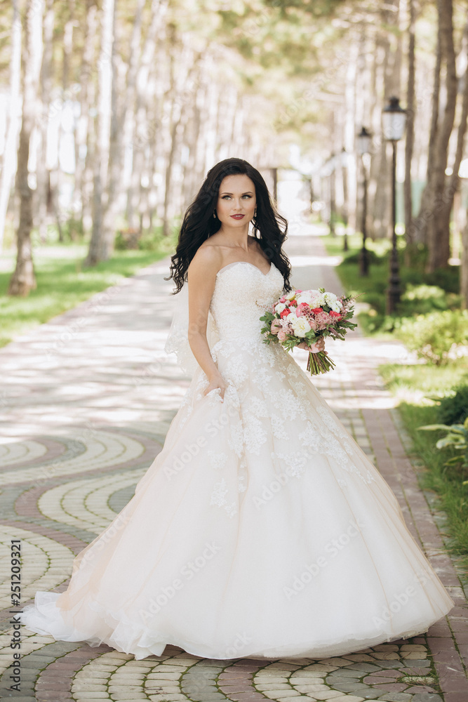 Beautiful bride in a white wedding dress on outdoors. Holding a wedding bouquet