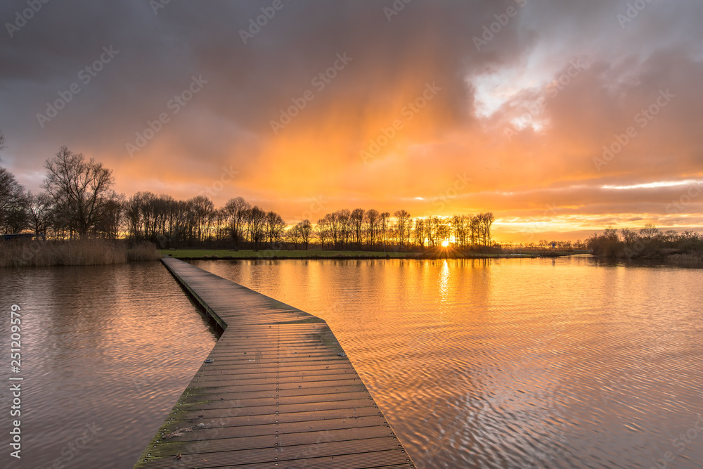 Wooden walkway in lake under orange sunset