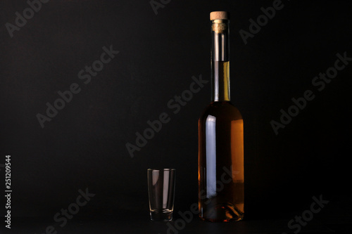 Bottles and glass with alcohol drink on black background. Homemade strong drink in transparent bottle on dark background. 