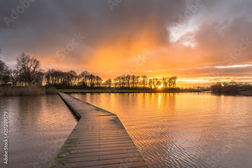 Wooden walkway in lake under orange sunset