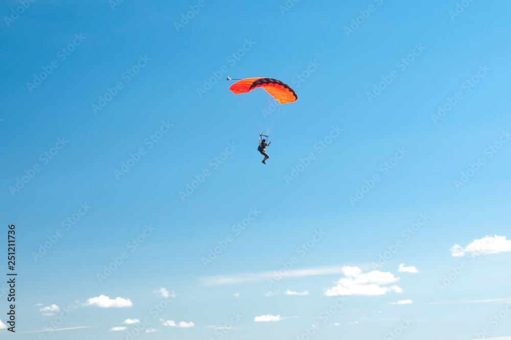 Parachutist soar on colorful parachutes across the boundless blue sky against the background of white fluffy clouds. Parachutist soar on colorful parachutes across the boundless blue sky against the background of white fluffy clouds.