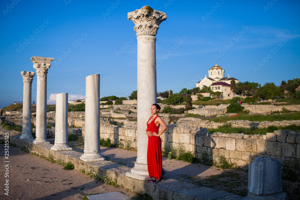 Φωτογραφία brunette girl in full growth in red dress among the ruins and colonnades
