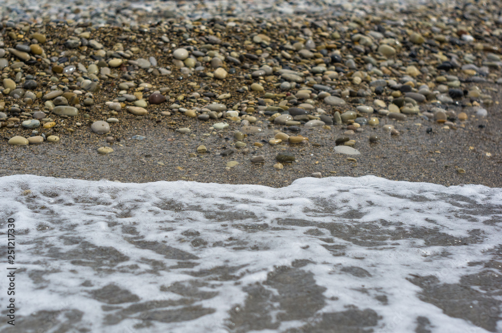 pebble stones on the sea beach, the rolling waves of the sea with foam