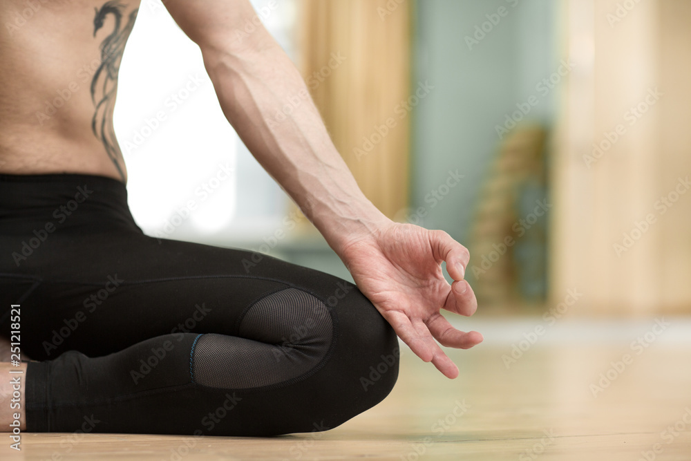Cropped close up shot of a tattooed shirtless man meditating while doing yoga at home. Close up of a male practicing yoga, relaxing after workout. Sportsman in lotus position close up