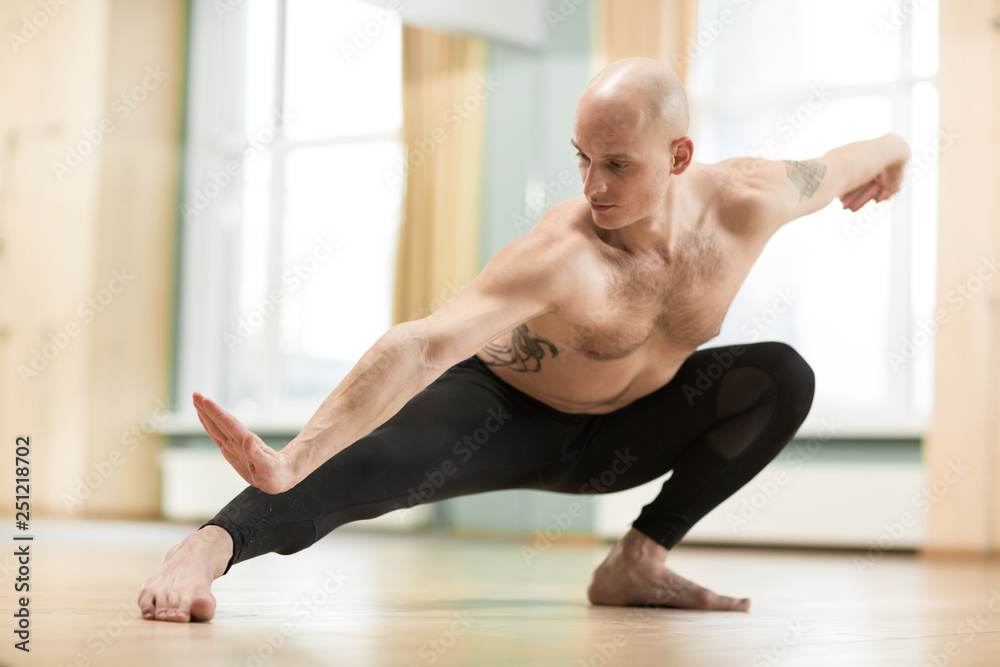 Horizontal shot of a young athletic man doing yoga at gym studio. Handsome shirtless sportsman practicing yoga, stretching indoors. Health, strength, motivation concept