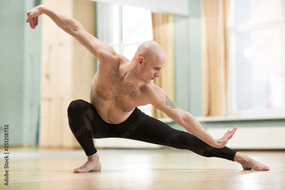 Fototapeta premium Young man working out shirtless doing stretching exercises at the gym studio. Handsome athletic man working out, practicing yoga. Healthy active lifestyle concept