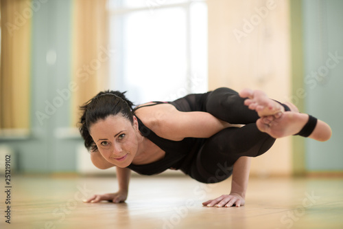 Shot of an attractive mature fitness female smiling joyfully to the camera doing handstand balancing yoga indoors. Gorgeous healthy sportswoman practicing yoga. Healthy active lifestyle concept