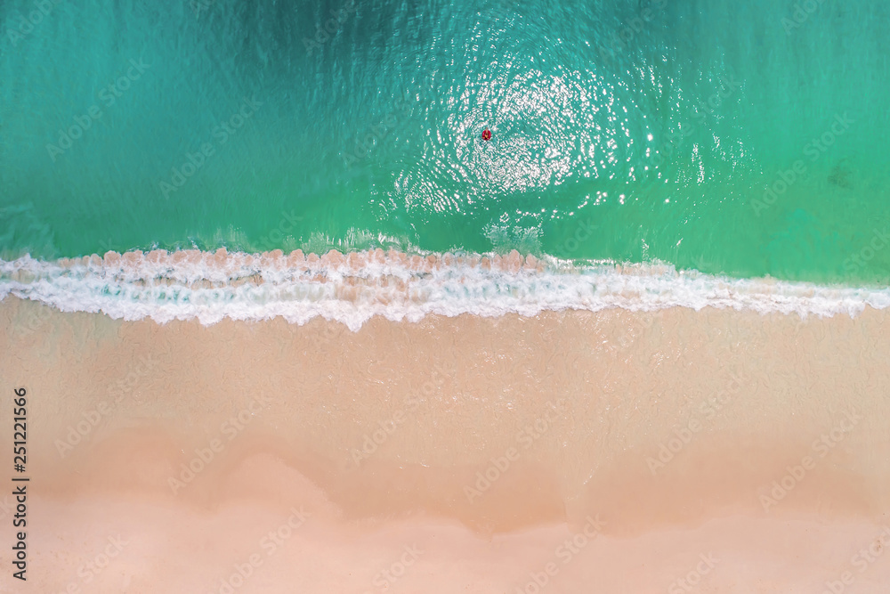 Fototapeta premium Aerial view of slim woman swimming on the swim ring donut in the transparent turquoise sea in Seychelles. Summer seascape with girl, beautiful waves, colorful water. Top view from drone
