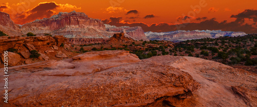 Sunset during golden hour in Southern Utah, sun warming red sandstone, cliffs, mountains, and mesa. With orange sky and red clouds