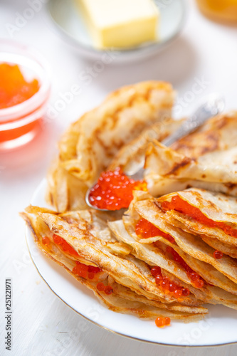 A stack of thin russian pancakes with caviar on a white plate