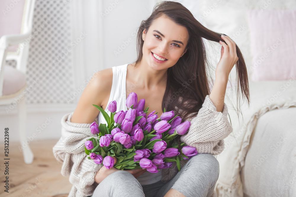 Attractive young woman with flowers indoors in the bedroom. Portrait of beautiful lady at home. Close up shot of female with tulips. Attractive young woman with flowers indoors in the bedroom. Portrait of beautiful lady at home. Close up shot of female with tulips.