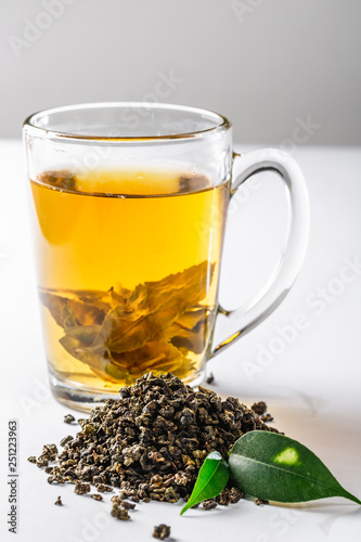 A Cup of green tea with dried large leaf tea and fresh tea leaves on a white background. Diet and healthy drink