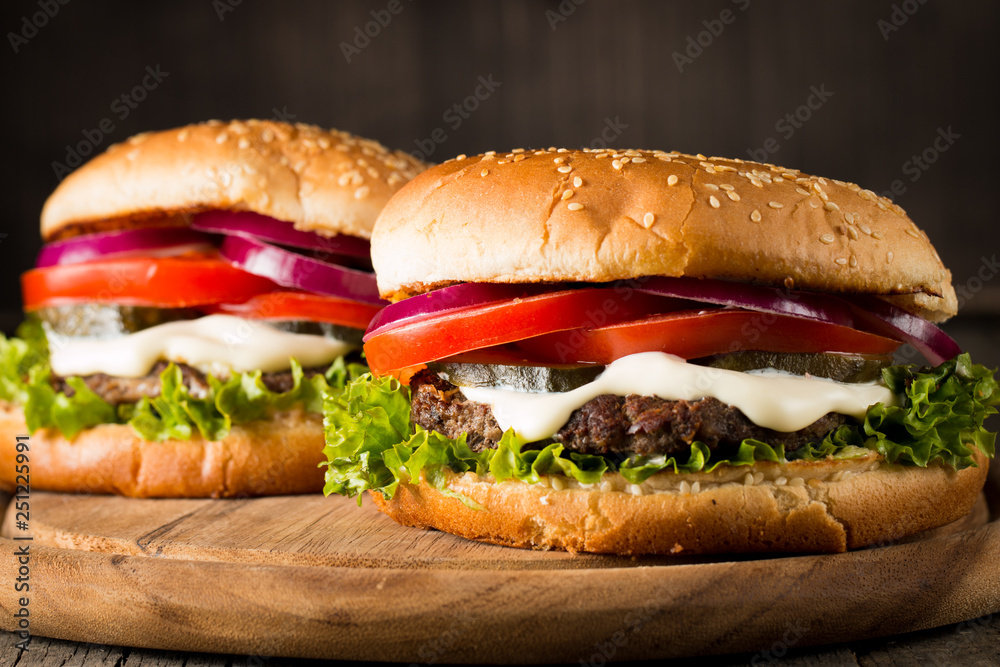 Close-up photo of home made hamburger with beer made of beef, onion, tomato, lettuce, cheese and spices. Fresh burger closeup on wooden rustic table with potato fries and chips. Close-up photo of home made hamburger with beer made of beef, onion, tomato, lettuce, cheese and spices. Fresh burger closeup on wooden rustic table with potato fries and chips.