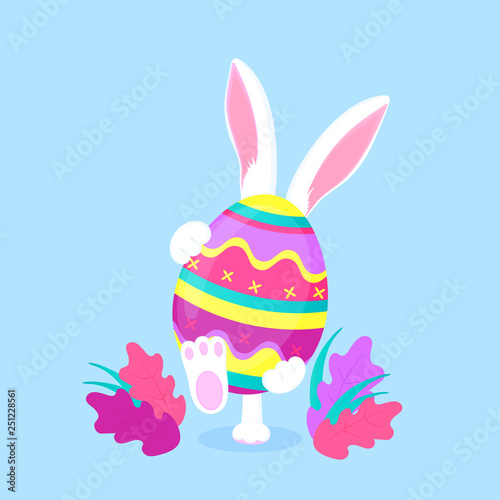 Easter bunny holding a big paschal egg. Funny rabbit walks on the lawn