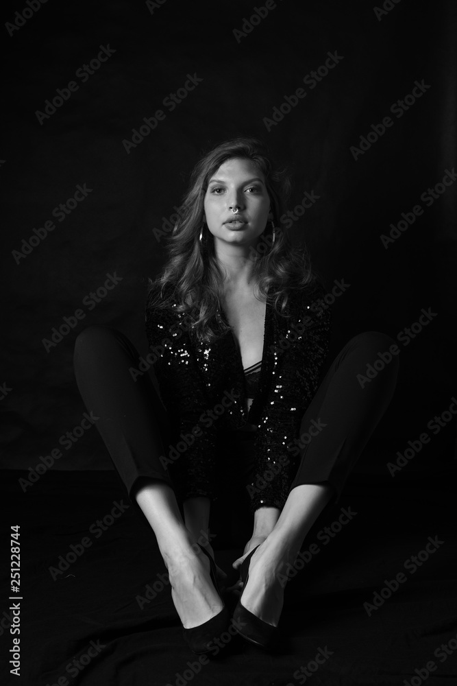 Black and white fashion photo of beautiful sexy woman with luxurious curly hair in elegant jacket with rhinestones posing in studio in front of black backgroung. Full-length girl model Black and white fashion photo of beautiful sexy woman with luxurious curly hair in elegant jacket with rhinestones posing in studio in front of black backgroung. Full-length girl model