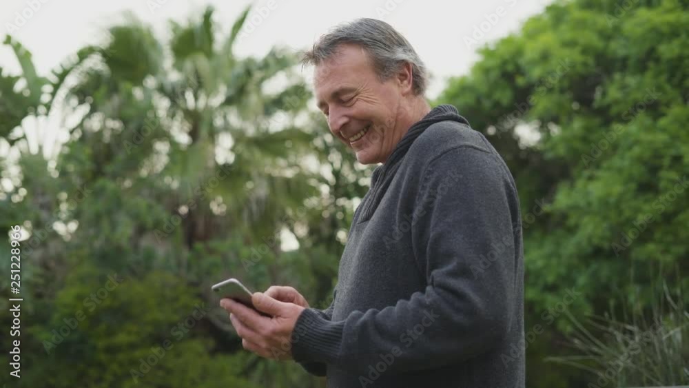Smiling happy mature man with grey hair using his smartphone in his garden Smiling happy mature man with grey hair using his smartphone in his garden