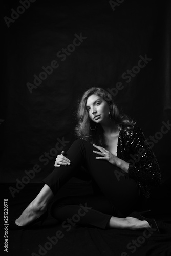 Black and white fashion photo of beautiful sexy woman with luxurious curly hair in elegant jacket with rhinestones posing in studio in front of black backgroung. Full-length girl model