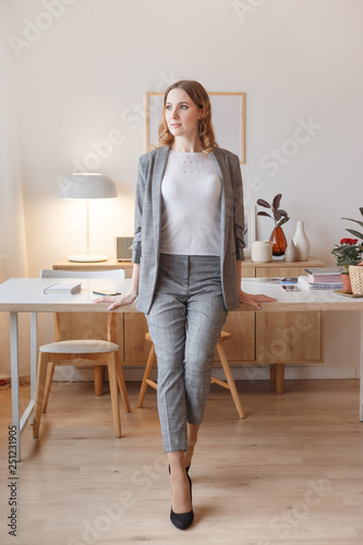 Young boss woman in a gray stylish suit stands in her own creative office