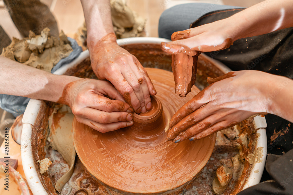 Master ceramist teaches student.Master ceramist teaches student. Craftsman hands making pottery bowl. Woman working on potter wheel . Family business shop sculpts pot from clay view top.