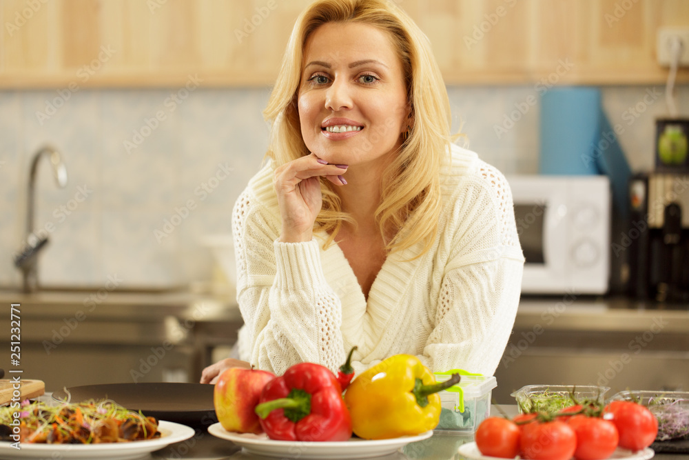Shot of a gorgeous happy mature woman smiling joyfully to the camera, posing at the kitchen at home. Cheerful housewife preparing to cook dinner for her family