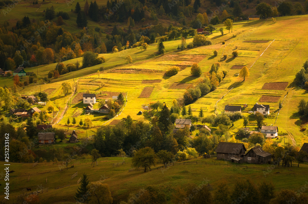 Naklejka premium Autumn pastoral landscape in morning light. Amazing rural landscape in autumn morning with wooden houses, fences and horses. Traditional view in Carpathians, Ukraine.