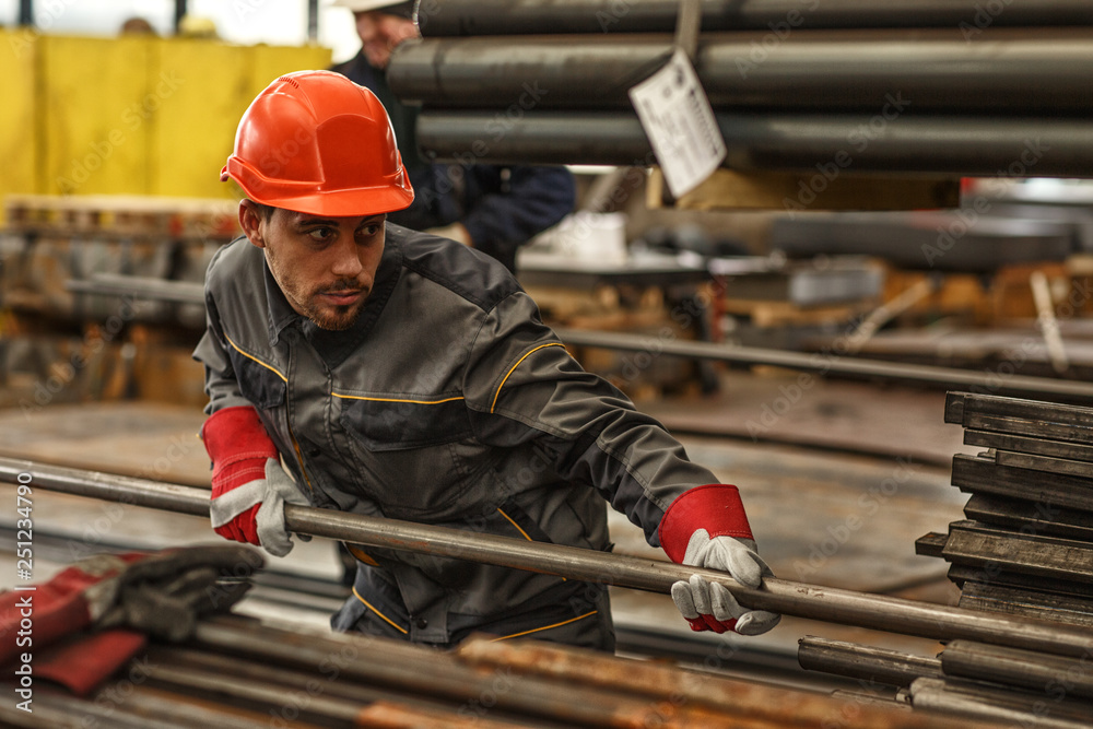 Horizontal shot of a handsome young warehouse manager organizing steel supplies wearing protective hardhat and uniform, copy space. Heavy industry, construction, engineering concept Horizontal shot of a handsome young warehouse manager organizing steel supplies wearing protective hardhat and uniform, copy space. Heavy industry, construction, engineering concept