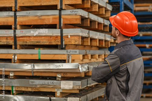 Horizontal rear view shot of a constructionist wearing hardhat and uniform checking pallets stacked at the warehouse, copy space. Import, export, logistics, shipping concept
